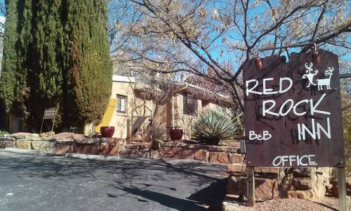 Sign for Red Rock Inn with office entrance, surrounded by trees and desert plants on a sunny day.