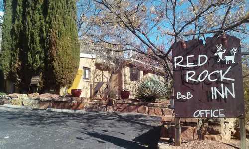 Sign for Red Rock Inn with office entrance, surrounded by trees and desert plants on a sunny day.