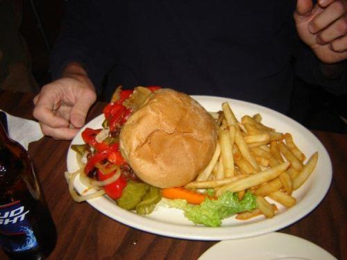 A plate with a large burger topped with vegetables, served with fries and pickles on the side.