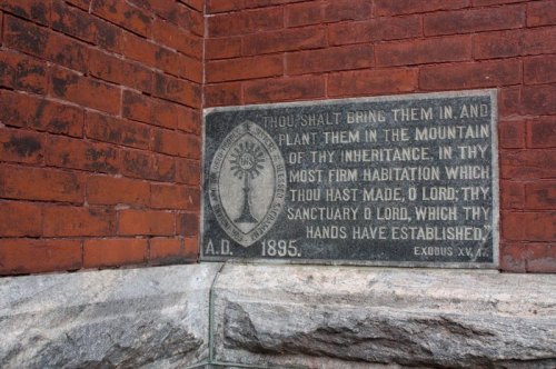 Plaque on a brick wall inscribed with a biblical verse and the year 1895.