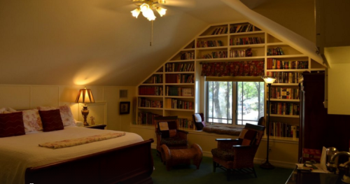 Cozy bedroom with a large bed, bookshelves, a reading nook by the window, and warm lighting.