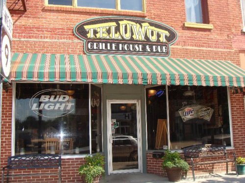 Exterior of Teluwut Grille House & Pub, featuring a brick facade, striped awning, and large windows displaying signage.