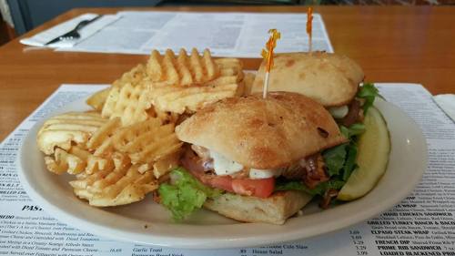 A plate with two sandwiches topped with lettuce, tomato, and sauce, accompanied by waffle fries and a pickle.