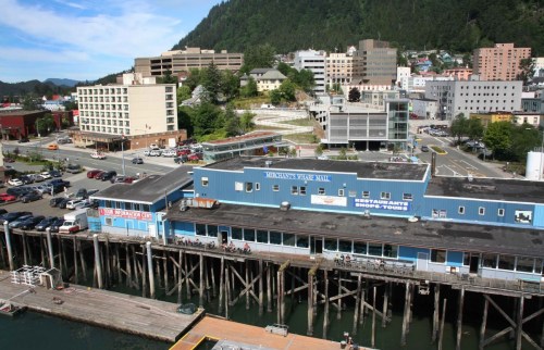 Aerial view of a waterfront area featuring buildings, a pier, and parked cars in a coastal town.