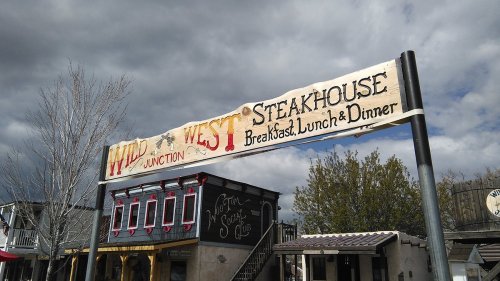 Sign for "Wild West Junction Steakhouse" advertising breakfast, lunch, and dinner, with a cloudy sky in the background.