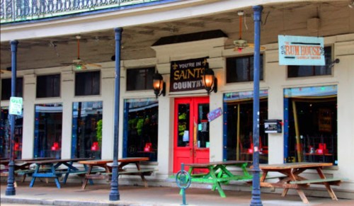 Colorful restaurant exterior with a red door, outdoor seating, and festive lights in a lively setting.