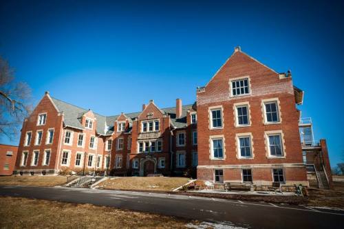 Historic brick building with multiple gables, set against a clear blue sky and grassy area in front.