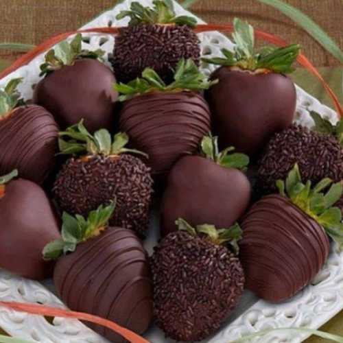 A plate of chocolate-covered strawberries, some with sprinkles, arranged with green leaves and decorative ribbon.