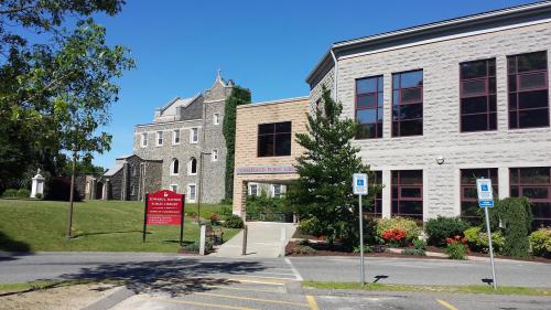 Exterior view of a public library building with stone and modern architecture, surrounded by greenery and a clear blue sky.