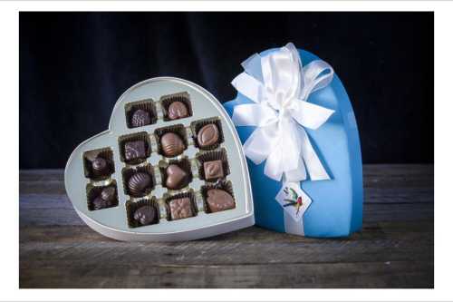 A heart-shaped box of assorted chocolates, partially open, with a blue exterior and white ribbon.