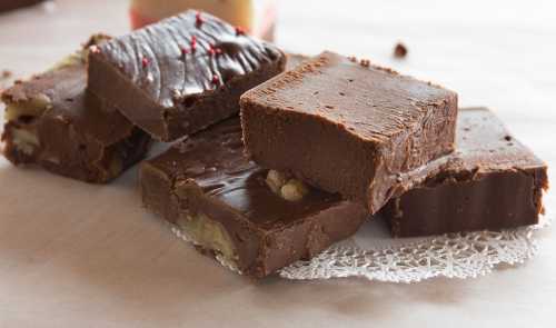 A close-up of assorted fudge pieces, including chocolate and nut varieties, arranged on a lace doily.