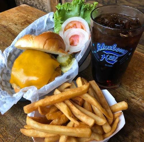 A cheeseburger with lettuce, tomato, and pickles, served with fries and a glass of iced drink.
