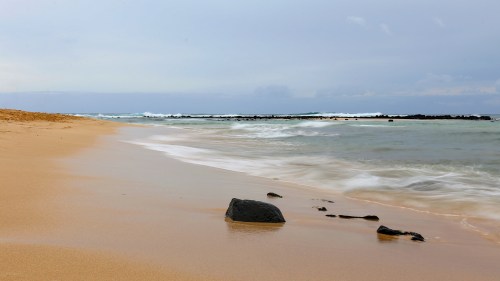 A serene beach scene with gentle waves lapping at the shore and smooth rocks scattered on the sandy beach.