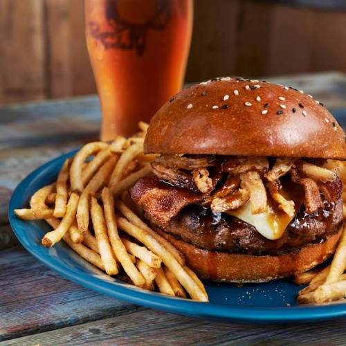 A juicy burger with bacon and cheese, served with crispy fries and a cold drink in a rustic setting.