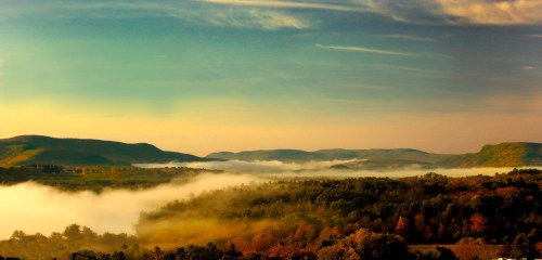 A serene landscape featuring rolling hills, fog, and a colorful autumn sky at sunrise.