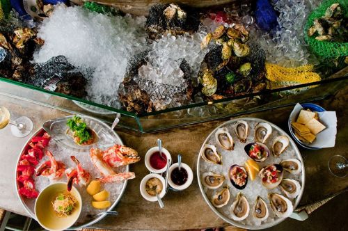 A seafood platter featuring oysters, shrimp, and lobster on ice, with sauces and garnishes, displayed elegantly.
