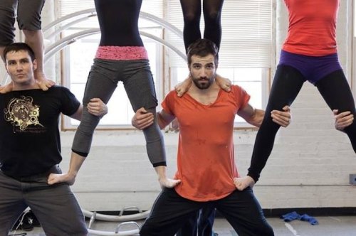 A group of five acrobats performing a human pyramid in a studio, showcasing strength and balance.