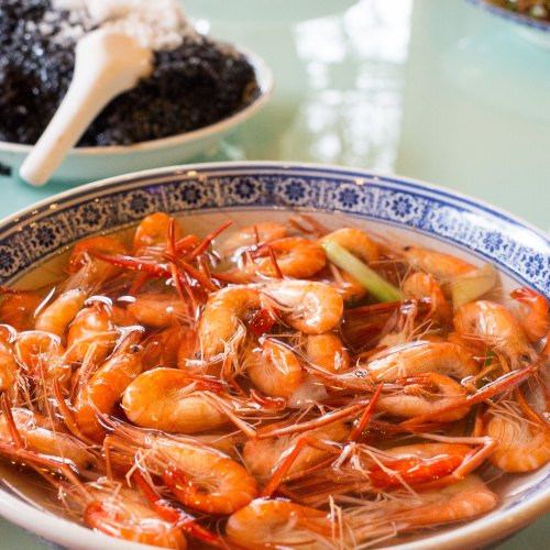 A bowl of cooked shrimp in broth, garnished with green onions, with a side of black seaweed in the background.
