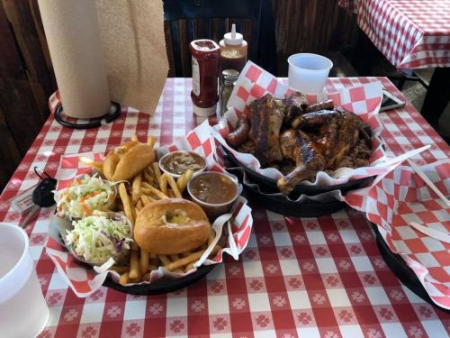 A table with two baskets of barbecue, fries, coleslaw, and a drink, set on a red-checkered tablecloth.