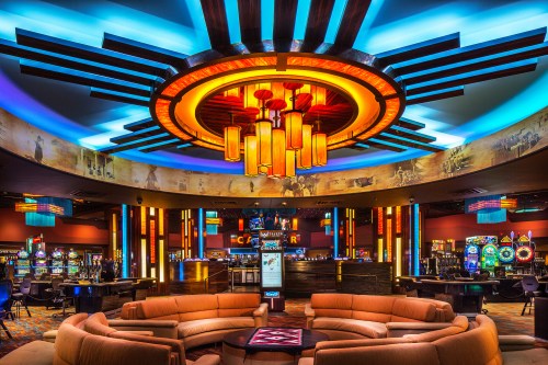 A vibrant casino interior featuring colorful lighting, a circular chandelier, and gaming tables with slot machines.
