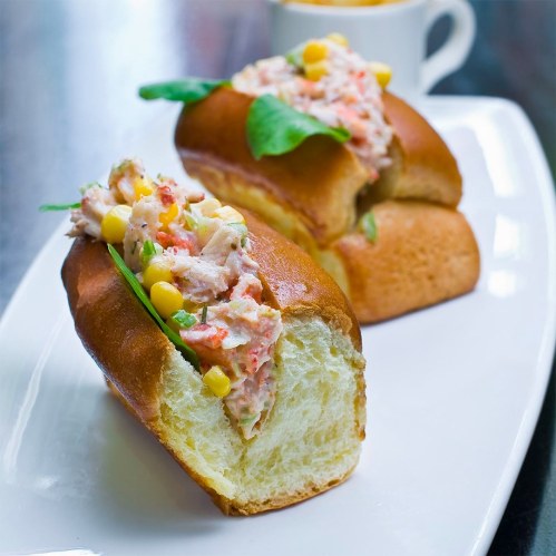 Two lobster rolls filled with creamy lobster salad, spinach, and corn, served on a white plate.