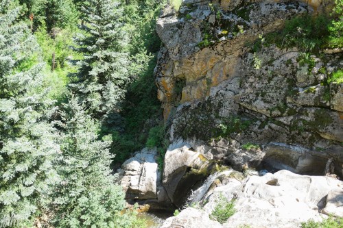 A rocky cliff surrounded by lush green trees and a small stream flowing through the landscape.
