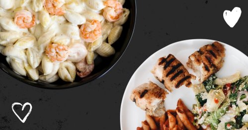 A bowl of creamy shrimp pasta beside a plate of grilled chicken, sweet potato fries, and a fresh salad.