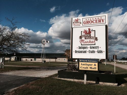Sign for Dutch Village Market featuring grocery, antiques, crafts, and a restaurant, with a windmill in the background.