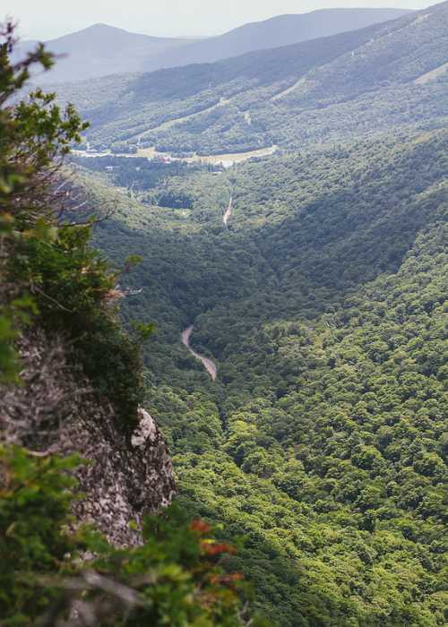 A lush green valley with winding roads and mountains in the background under a clear sky.