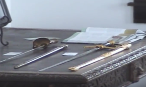 A wooden table displaying several ornate swords and a book in the background.