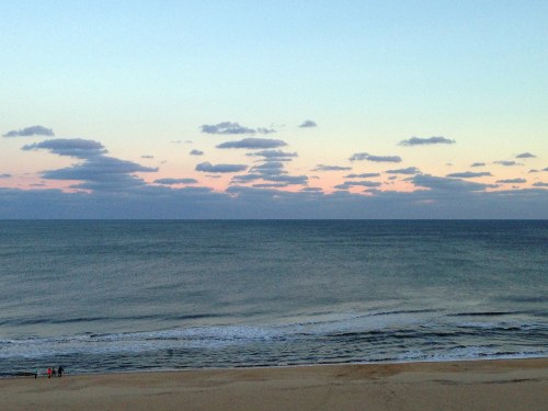 A serene beach scene at dusk, with gentle waves and a colorful sky filled with clouds.