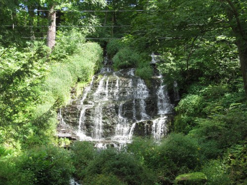 A serene waterfall cascading down rocky steps, surrounded by lush green foliage and trees.