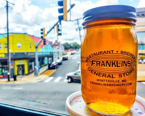 A jar of amber liquid sits on a windowsill, overlooking a colorful street scene in Hyattsville, MD.