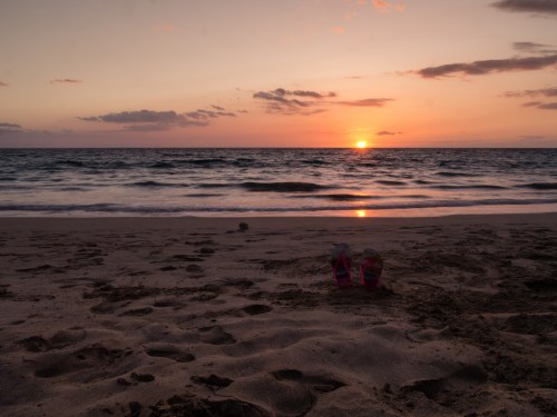 A serene beach at sunset, with gentle waves and a pair of shoes resting in the sand.