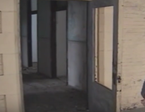 An empty, dimly lit hallway with doorways leading to other rooms in a worn, abandoned building.