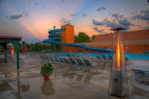 A vibrant pool area at sunset, featuring a water slide, lounge chairs, and a heater, with colorful clouds in the sky.