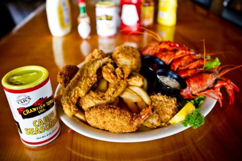 A plate of fried seafood, including crawfish, fish, and fries, with a can of Cajun seasoning in the foreground.