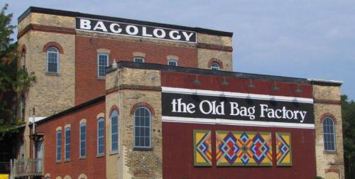 Historic brick building with "Bagology" and "the Old Bag Factory" signs, featuring colorful geometric artwork.