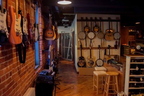 A music store interior featuring various guitars and banjos displayed on brick walls and wooden floors.
