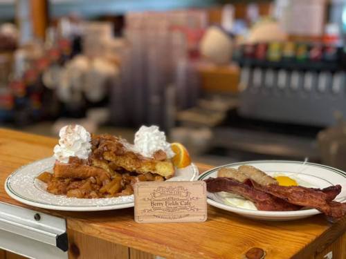 A plate of French toast topped with whipped cream and fruit, alongside a plate of bacon and eggs, with a café sign.