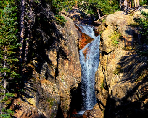 A serene waterfall cascading down rocky cliffs, surrounded by lush green trees and sunlight filtering through.