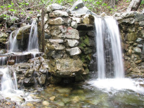 A serene scene of a rocky waterfall cascading into a clear pool, surrounded by lush greenery.