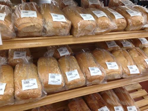 A display of various loaves of bread, all packaged and labeled, arranged neatly on wooden shelves.