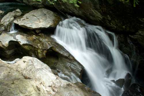 A serene waterfall cascading over smooth rocks in a lush, green forest setting.