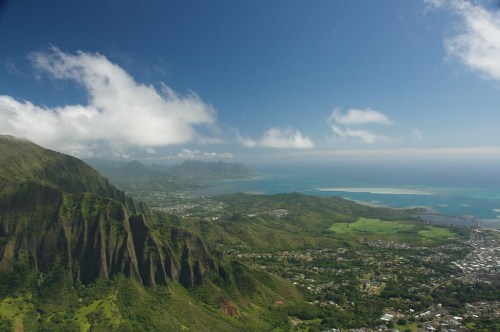 Aerial view of lush green mountains and coastline under a blue sky with scattered clouds.