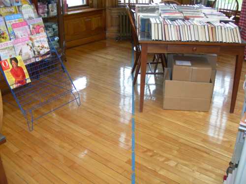 A wooden floor in a room with a magazine rack, a table with books, and a cardboard box.