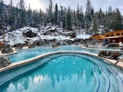 A serene hot spring pool surrounded by snowy trees and rocky terrain, with steam rising in a tranquil setting.