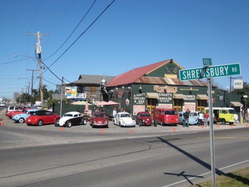A vintage car show outside a grocery store and bar, with colorful classic cars parked along the street.