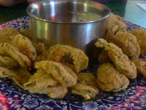 A plate of crispy fried pickles with a small bowl of dipping sauce in the center.