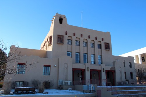 Historic adobe-style building with a flat roof and decorative elements, set against a clear blue sky.